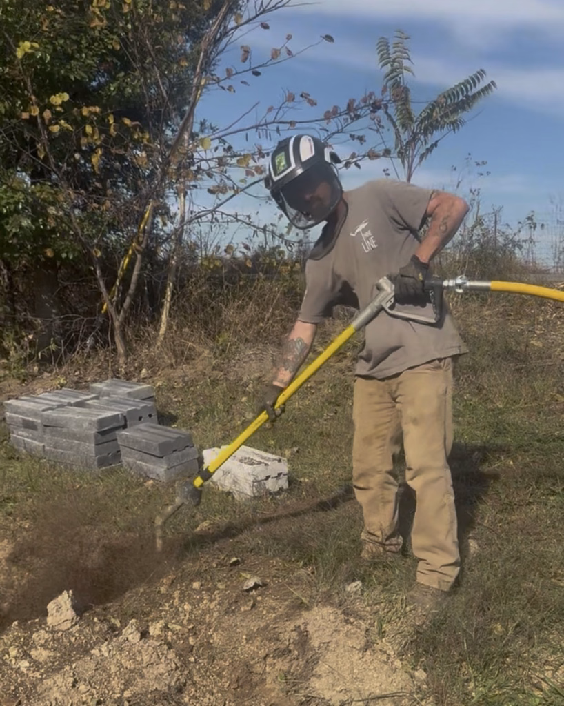 Arborist using a pneumatic air excavation tool to decompact soil and expose tree roots.